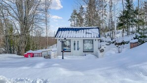 Une petite cabane blanche, coiffée d’un toit bleu, est entourée d’arbres couverts de neige.
