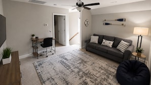 Una sala de estar con sofá, escritorio, silla, puf, televisor y ventilador de techo.