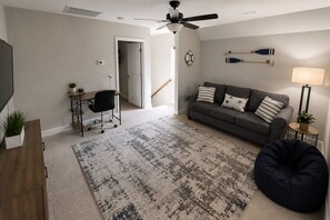 Una sala de estar con sofá, escritorio, silla, puf, televisor y ventilador de techo.
