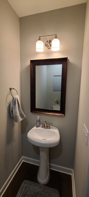 A bathroom with a pedestal sink, a mirror with a dark frame, and a towel hanging on a rack.