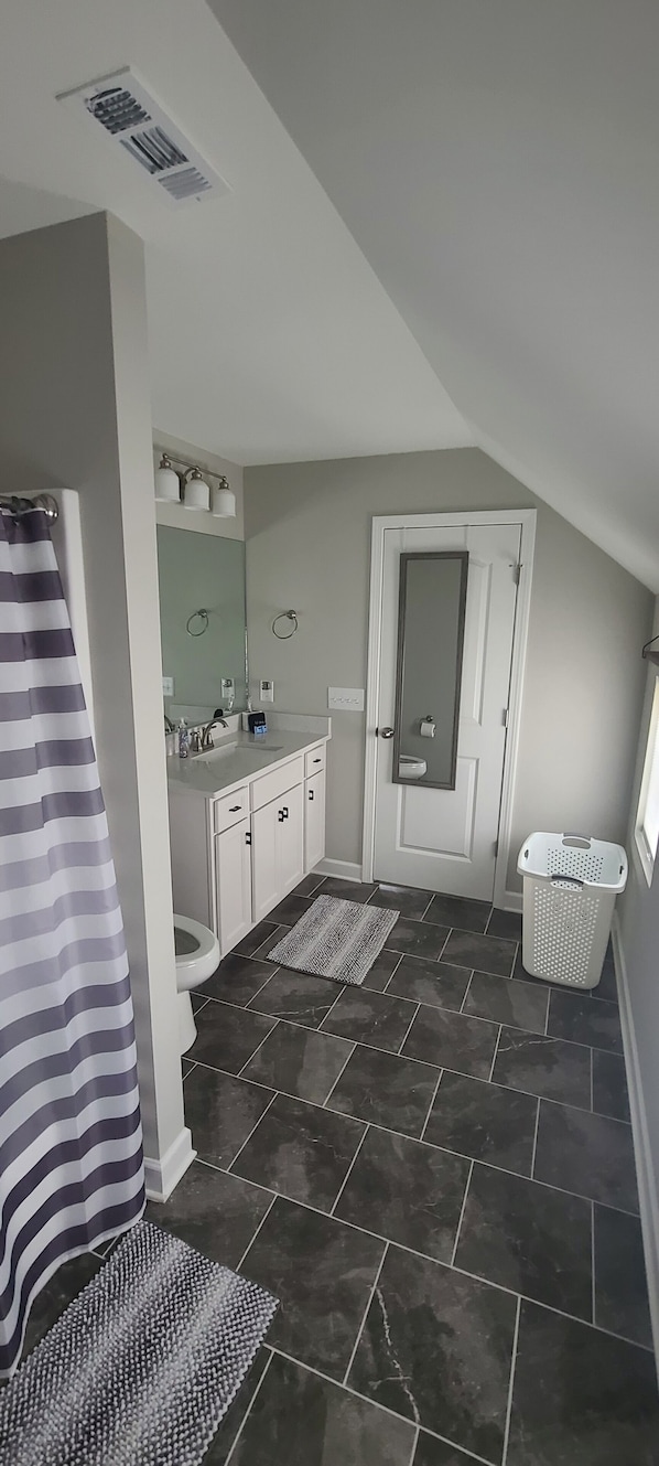 A bathroom with a toilet, sink, and mirror. There is a shower curtain and a laundry basket.