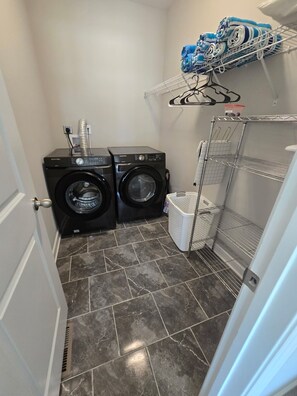 A laundry room with two front-loading washers, a drying rack, a basket, and a shelving unit with folded towels.
