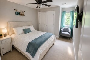 A bedroom with a bed, nightstand, lamp, ceiling fan, and a chair.