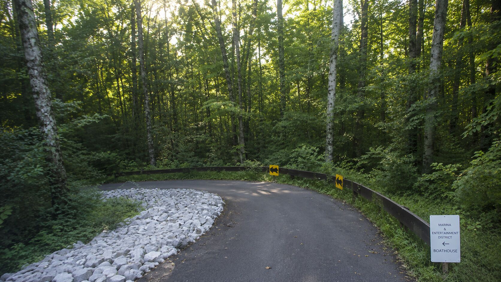 A winding road in a forested area with a sign indicating a marina and entertainment district.
