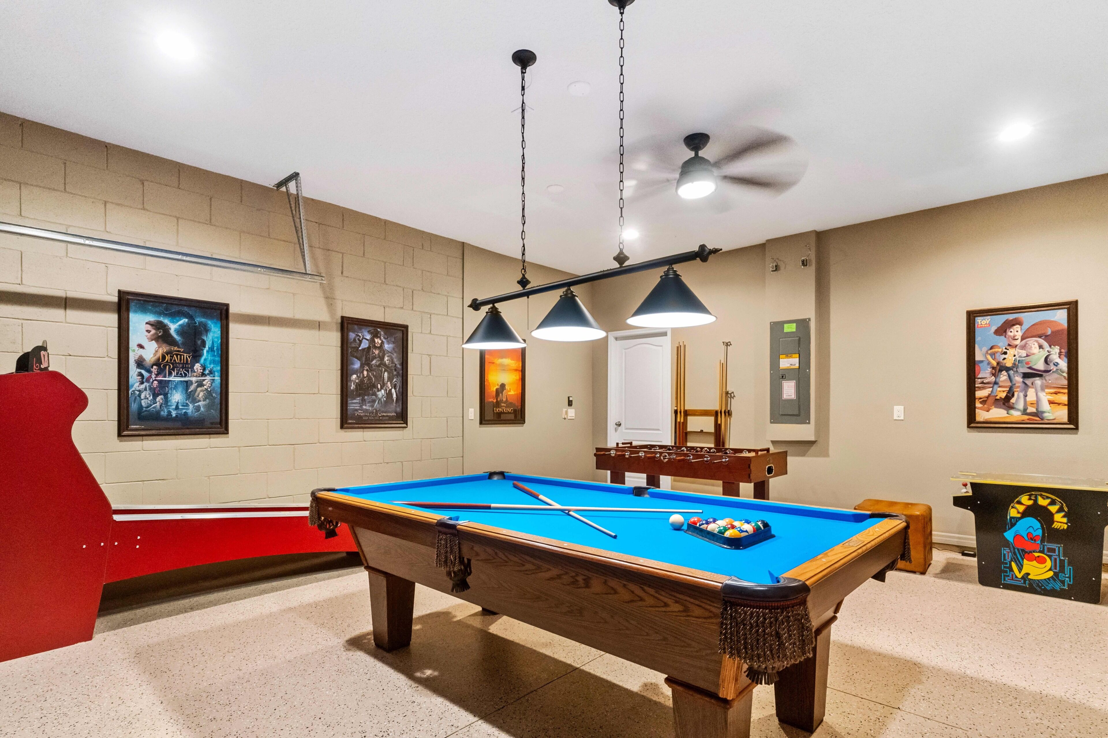 A pool table with a blue felt surface, overhead lighting, and a ceiling fan.