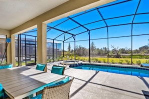 An outdoor pool area with a glass enclosure, a table with chairs, and a hot tub. - 7663 Oakmoss Loop (Davenport)