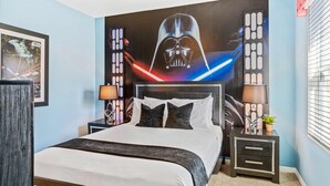 A bedroom with a Star Wars themed headboard, a bed with white and dark bedding, two bedside tables with lamps, and a window with blinds. - 7663 Oakmoss Loop (Davenport)