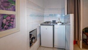 Uma cozinha compacta com azulejos brancos, fogão a gás, pia e geladeira pequena.