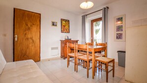 Quarto com porta de madeira, mesa de jantar com quatro cadeiras, pequena cozinha e uma cama.