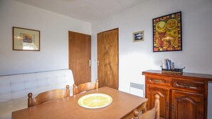 Uma sala de jantar com mesa de madeira, cadeiras, um sofá e um aparador com livros.