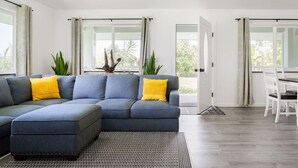 A modern living room with a sectional sofa, a dining table, and a view of the outdoors. - NEW - Lauhala - Hawaiian Villa with private hot tub (Keaau)