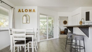 A modern kitchen with white cabinetry, a black countertop, and a dining area with white chairs. - NEW - Lauhala - Hawaiian Villa with private hot tub (Keaau)