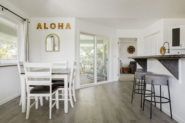 A modern kitchen with white cabinetry, a black countertop, and a dining area with white chairs.