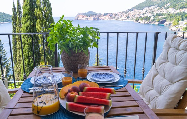 A balcony with a table set for breakfast, overlooking a coastal town. - Cozy apartment in Dubrovnik with WiFi (Dubrovnik)