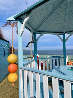 Um deck de madeira com um gazebo, um balanço de corda e vista para o mar.