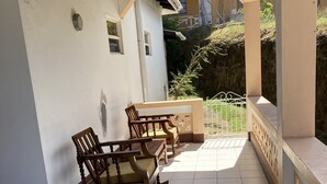 Un patio cubierto con piso de baldosas, una mecedora de madera, una mesita y una baranda de metal.