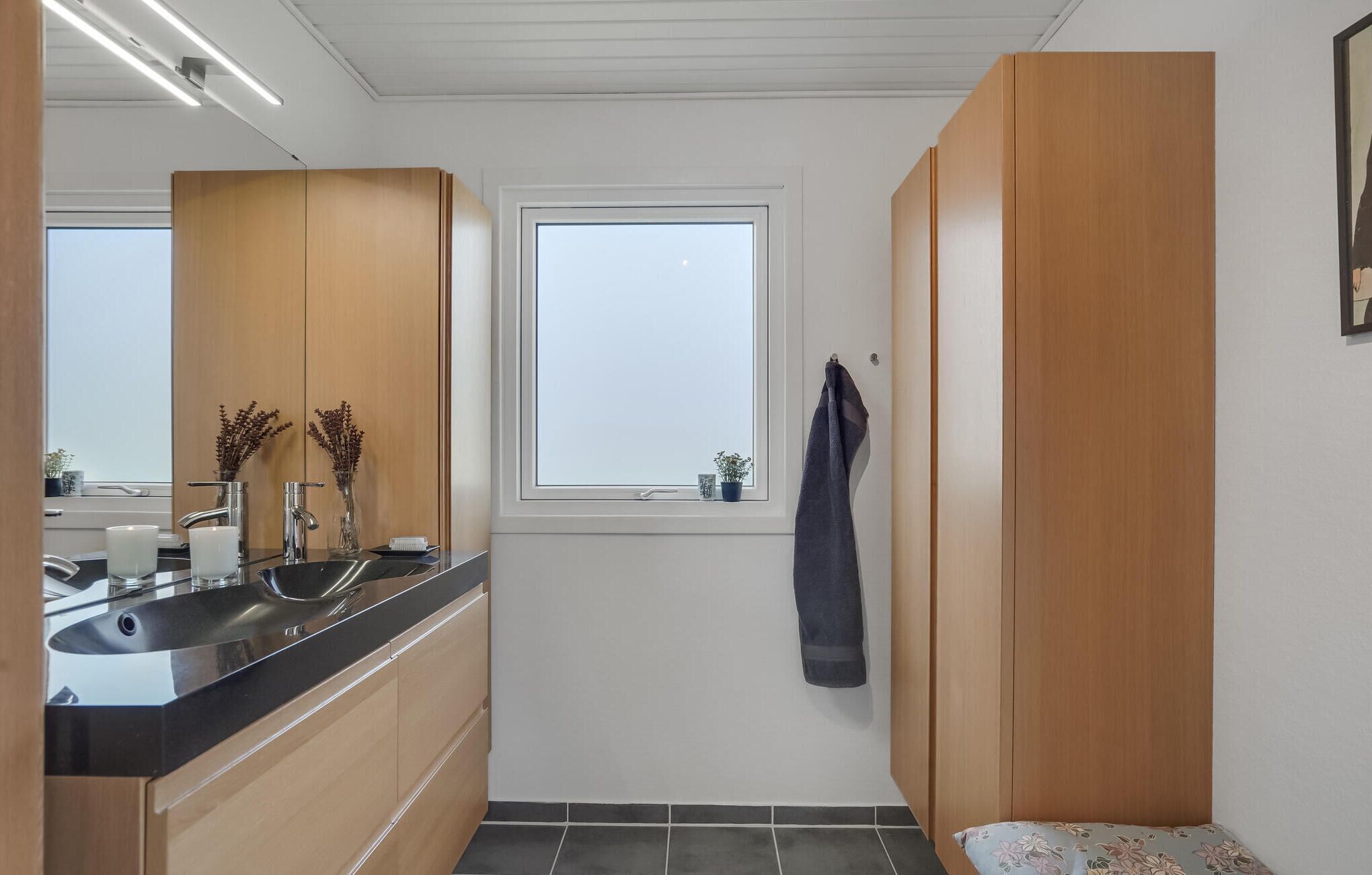 Une salle de bain moderne avec un lavabo, un miroir, des meubles en bois et une fenêtre.