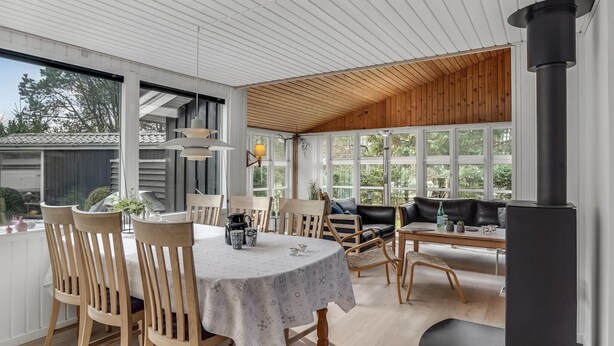 A sunlit room with a round table, wooden chairs, a sofa, and a black stove. - 3 bedroom beautiful home in Hals (Hals)