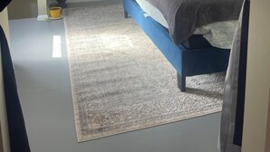 Une chambre à coucher avec un lit, un ventilateur de plafond, une télévision, une fenêtre avec des rideaux, une plante et un tapis.