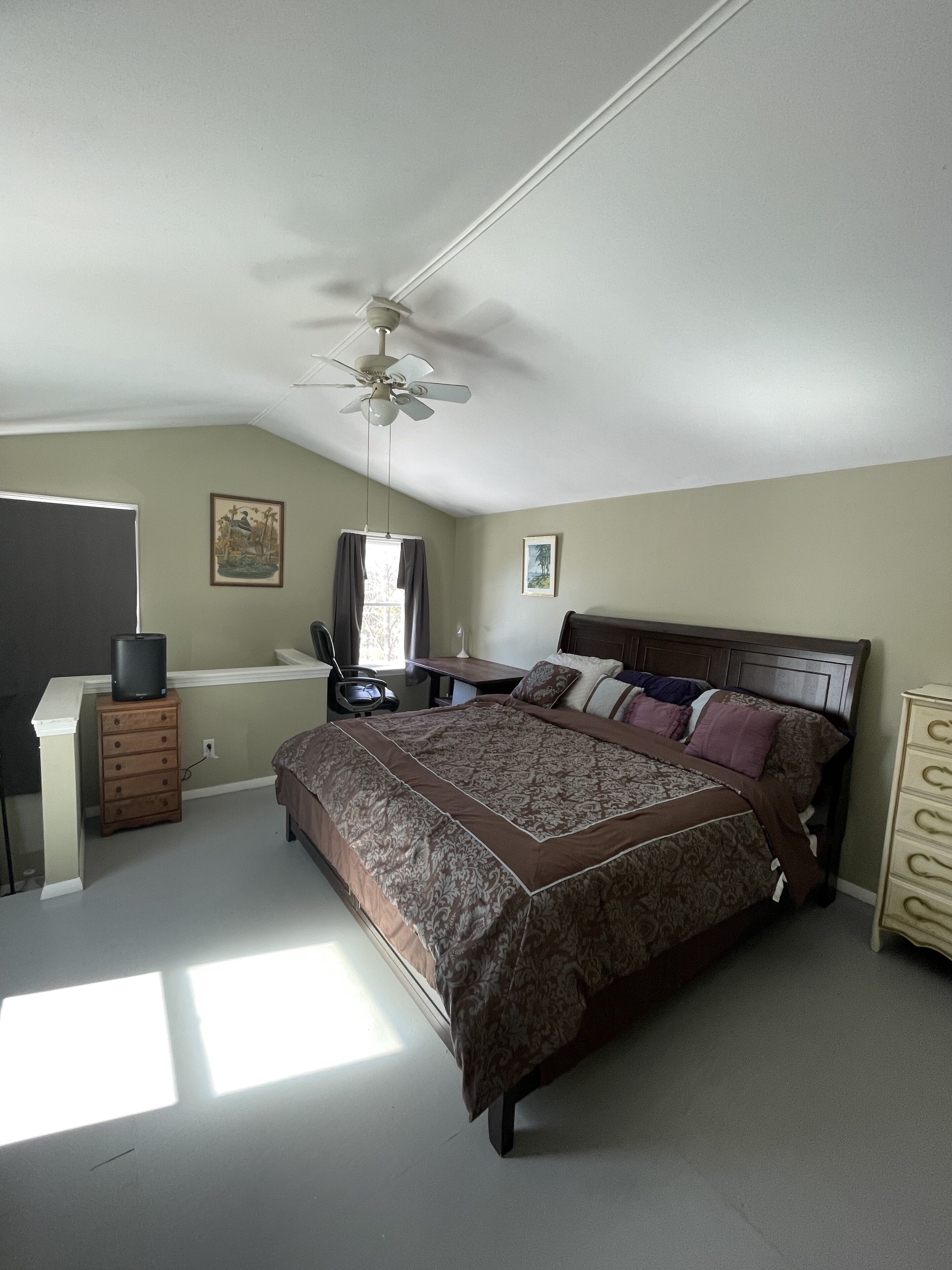 Un dormitorio con cama, escritorio, silla, cómoda, ventilador de techo y ventana.