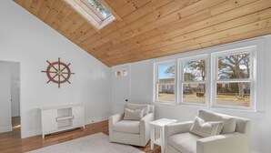 A spacious room with a high wooden ceiling, white walls, and large windows offering a view of the outside. - Newly Renovated Beach House w/ Central AC - 5min walk to the beach (Dennis)