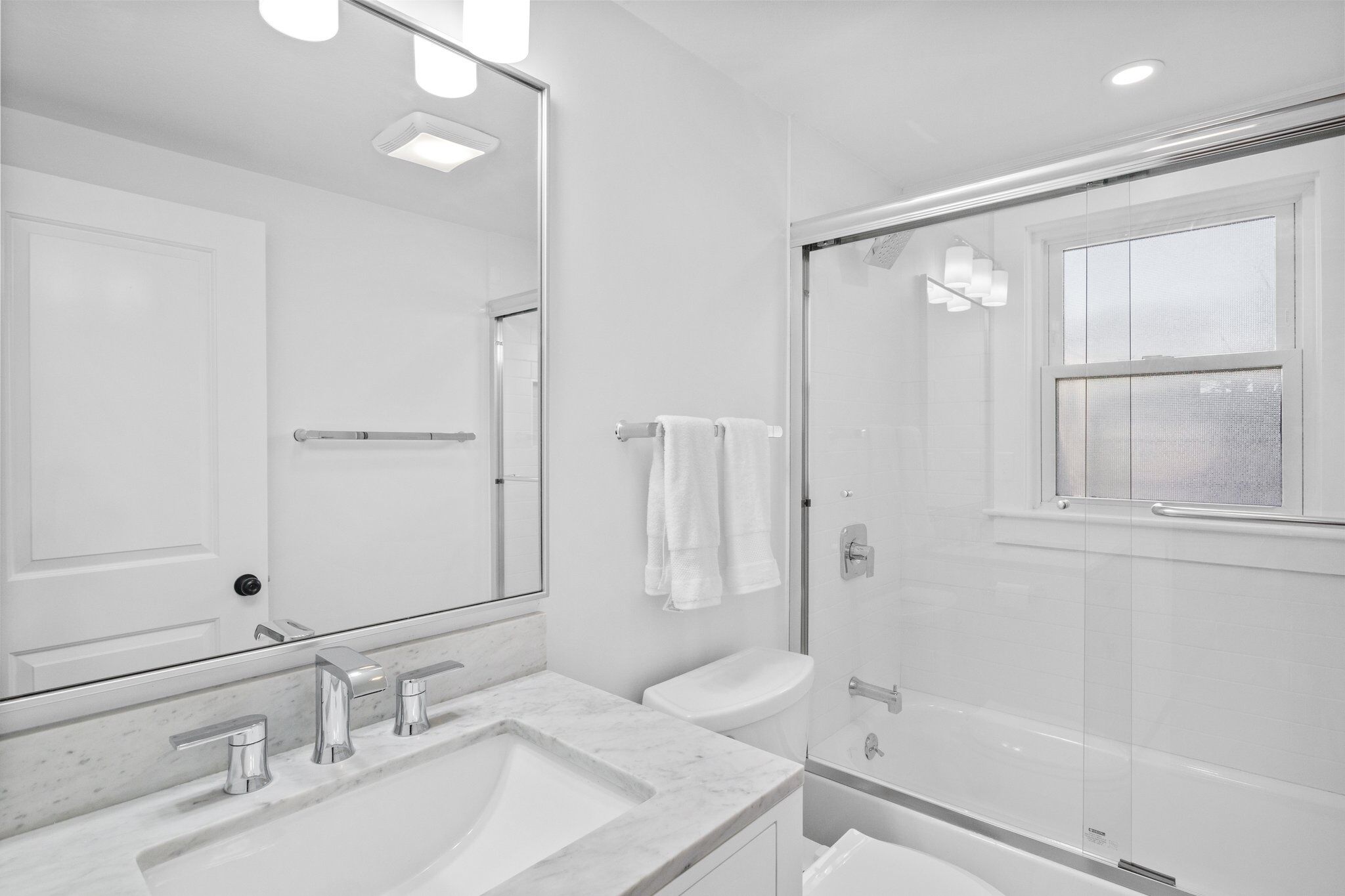 Une salle de bain moderne avec un grand miroir, un lavabo à deux robinets, des toilettes et une douche à parois de verre.