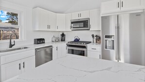 A modern kitchen with white cabinetry, stainless steel appliances, and a marble countertop. - Newly Renovated Beach House w/ Central AC - 5min walk to the beach (Dennis)