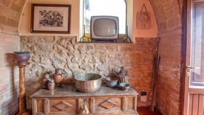 Una cucina rustica con parete in pietra, pensili in legno e un televisore d'epoca.