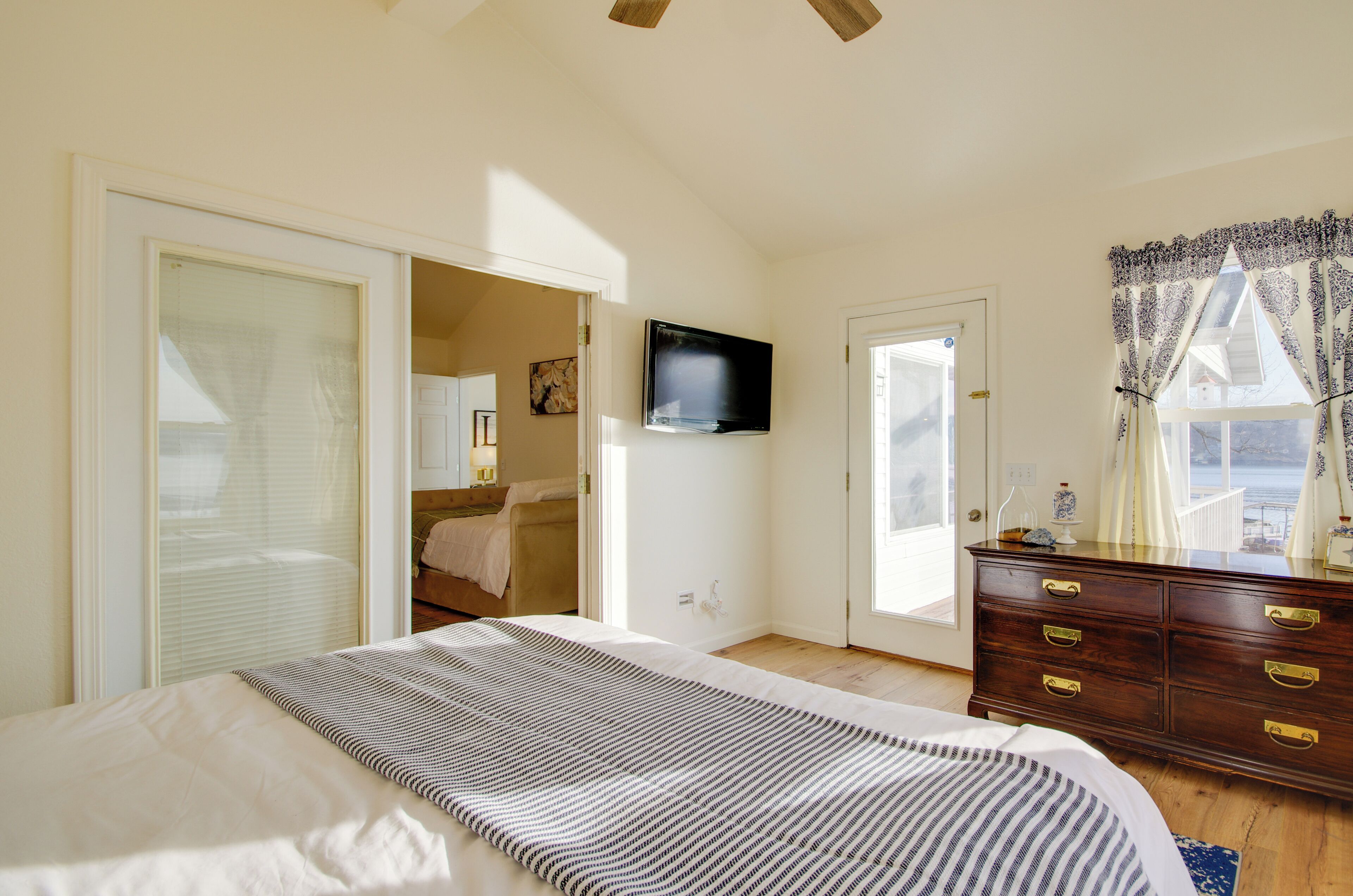 Une chambre à coucher comprenant un lit, une commode, un téléviseur et donnant sur l’extérieur.
