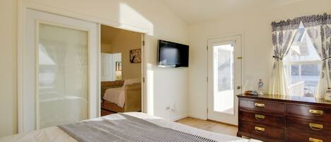 Une chambre à coucher comprenant un lit, une commode, un téléviseur et donnant sur l’extérieur.