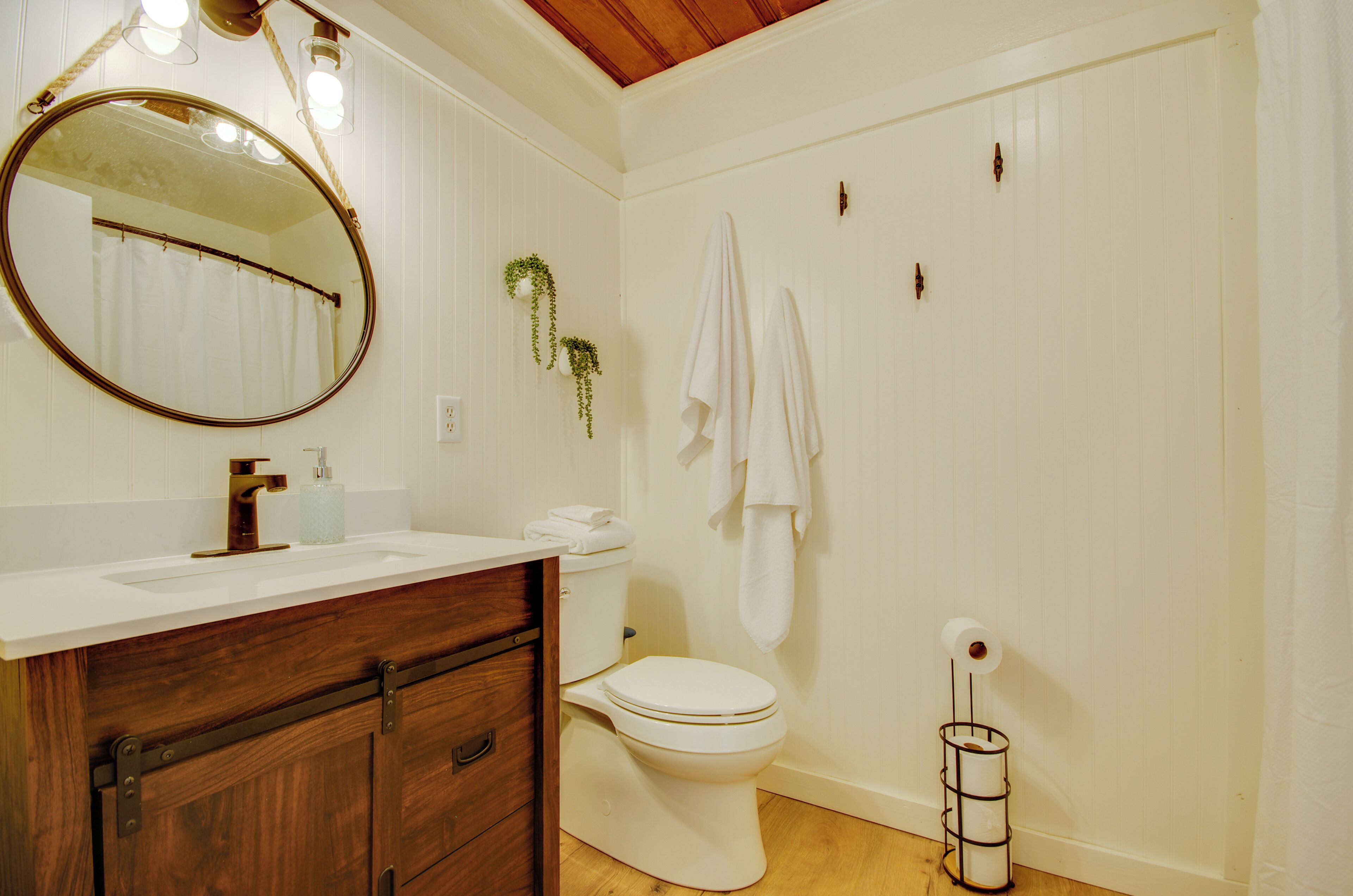 A bathroom with a wooden vanity, a round mirror, a toilet, and a hanging towel rack.