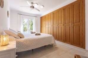 A bedroom with a bed, a ceiling fan, wooden wardrobe, and a window with curtains.
