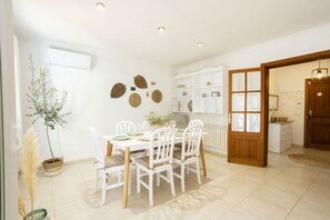 Un comedor con sillas blancas y una mesa, un armario blanco con estantes, y una puerta de madera.
