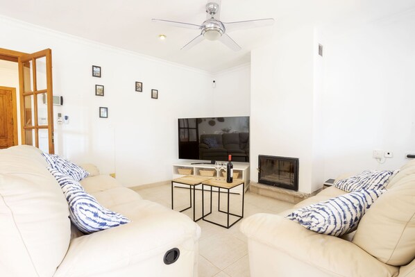 A living room with two beige sofas, a wooden coffee table, a flat-screen TV, and a fireplace. - 4 bedroom country house with pool and barbecue (Bunyola)