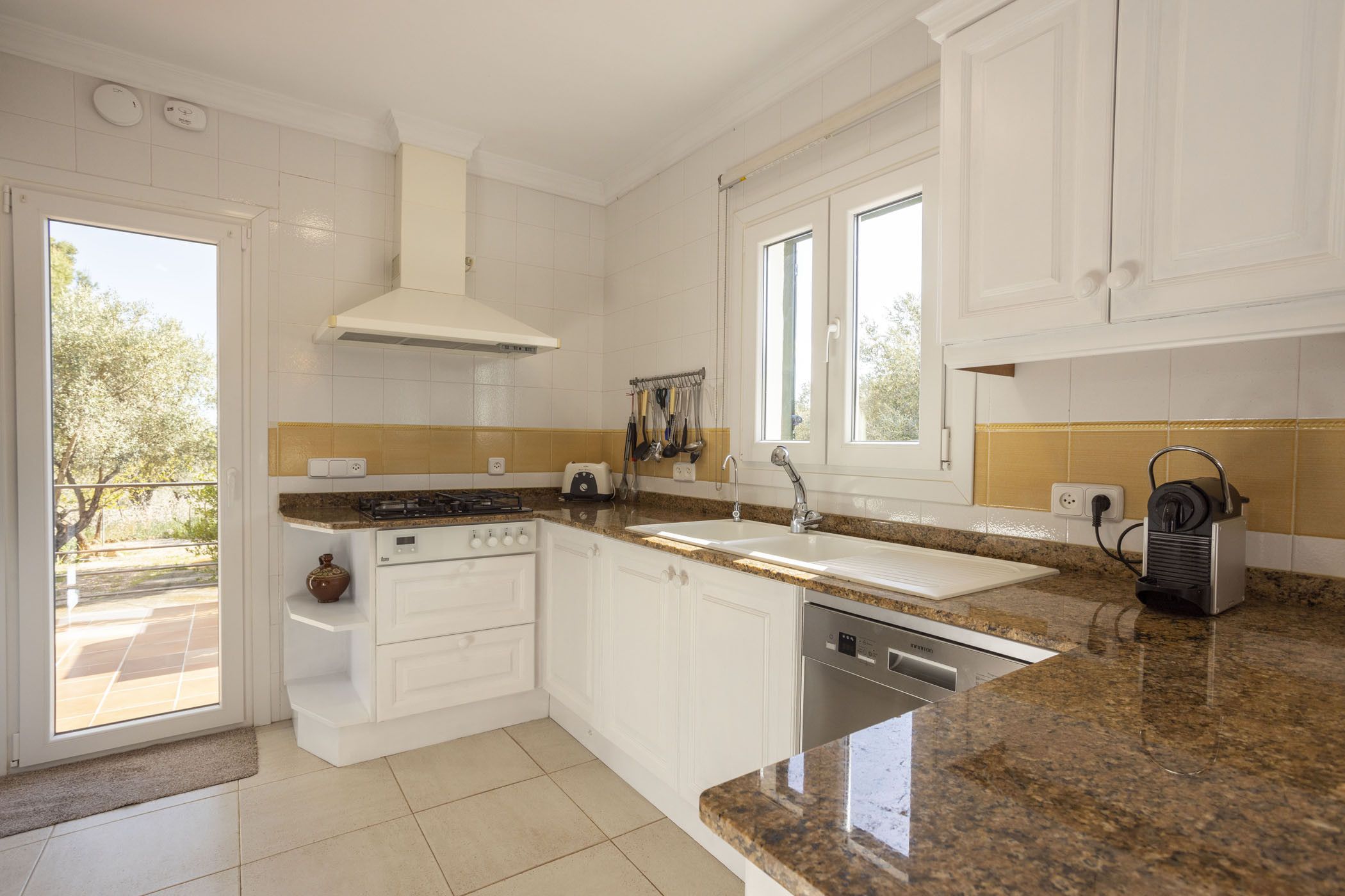 A modern kitchen with white cabinets, granite countertops, a built-in oven, and a dishwasher.