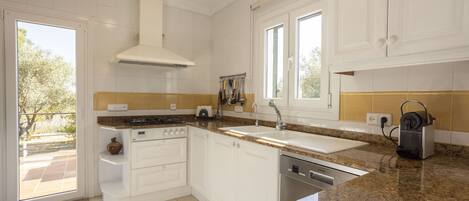 A modern kitchen with white cabinets, granite countertops, a built-in oven, and a dishwasher.