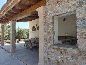 An outdoor patio with a stone wall, a wooden pergola, a table with chairs, and hanging lights. - 4 bedroom country house with pool and barbecue (Bunyola)