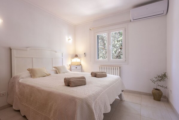 Un dormitorio con cama, mesitas de noche, un radiador y una ventana.