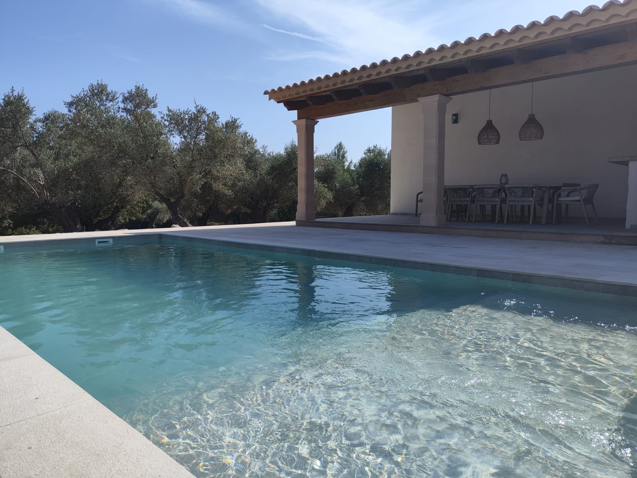 Una piscina cristalina con un pérgola y zona de estar al aire libre.