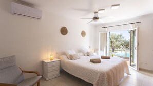 A bedroom with a bed, bedside table, chair, and a view of a pool through a sliding door. - 4 bedroom country house with pool and barbecue (Bunyola)
