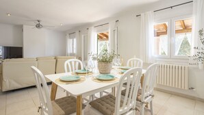 A dining area with a white table set for six, surrounded by white chairs with brown cushions. A ceiling fan is visible above, and a radiator is on the wall to the right. - 4 bedroom country house with pool and barbecue (Bunyola)