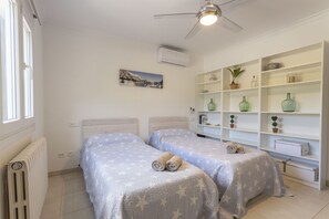 A bedroom with two beds, a ceiling fan, a radiator, and a shelving unit with decorative items. - 4 bedroom country house with pool and barbecue (Bunyola)