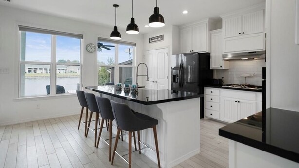 A modern kitchen with white cabinets, a black countertop, and three pendant lights. - New Waterfront House with Golf Cart!  (Montgomery)