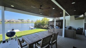 A covered patio with a wooden table and chairs, a grill, and a view of a lake. - New Waterfront House with Golf Cart!  (Montgomery)