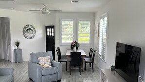 A modern living room with a grey sofa, a coffee table, and a TV on a cabinet. There is a dining area with a table and chairs, and a ceiling fan. - New Waterfront House with Golf Cart!  (Montgomery)