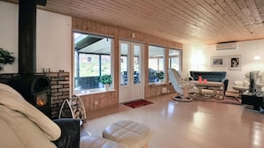 En hyggelig stue med pejs, trævægge og store vinduer.