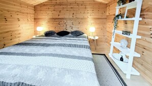 Et hyggeligt træværelse med en seng, to sengeborde med lamper, en hvid reol med pynteting og et lille bord med en lampe.