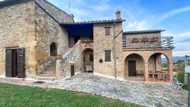 A stone building with a staircase leading to a second level, featuring arched doorways and a balcony with potted plants. - Lovely apartment in Volterra with WiFi (Volterra)