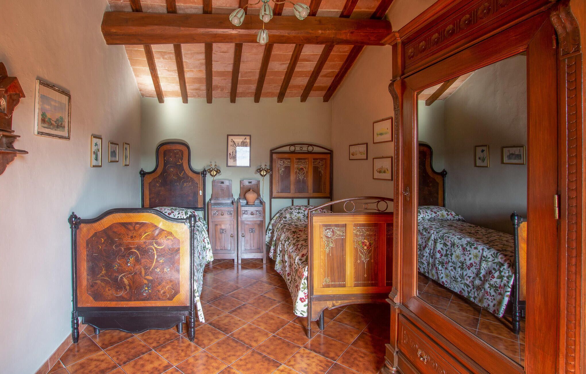 Un dormitorio tradicional con techo de madera, dos camas de madera con colchas florales, un espejo grande y un armario de madera.