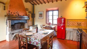 A rustic kitchen with a stone fireplace, wooden beams, a red refrigerator, and a dining table set for four. - Lovely apartment in Volterra with WiFi (Volterra)